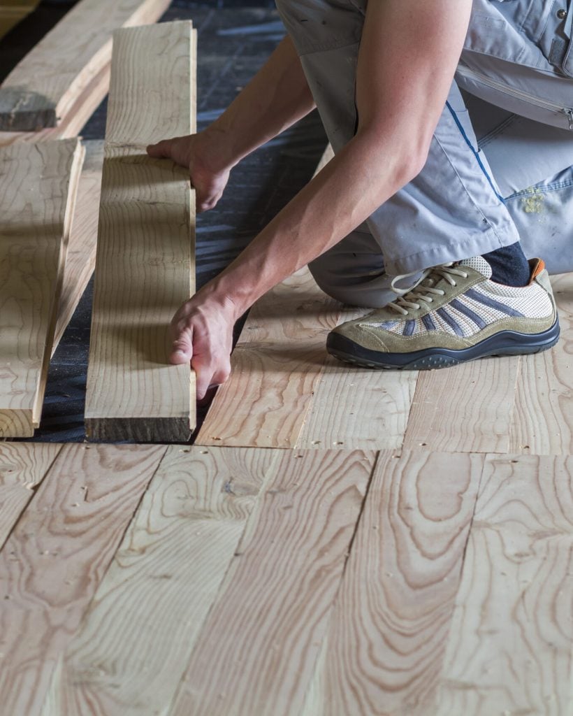 Close up of professional carpenter installing natural wooden new planks on cement floor in empty unfinished room under reconstruction. Improvement, renovation and carpentry concept.